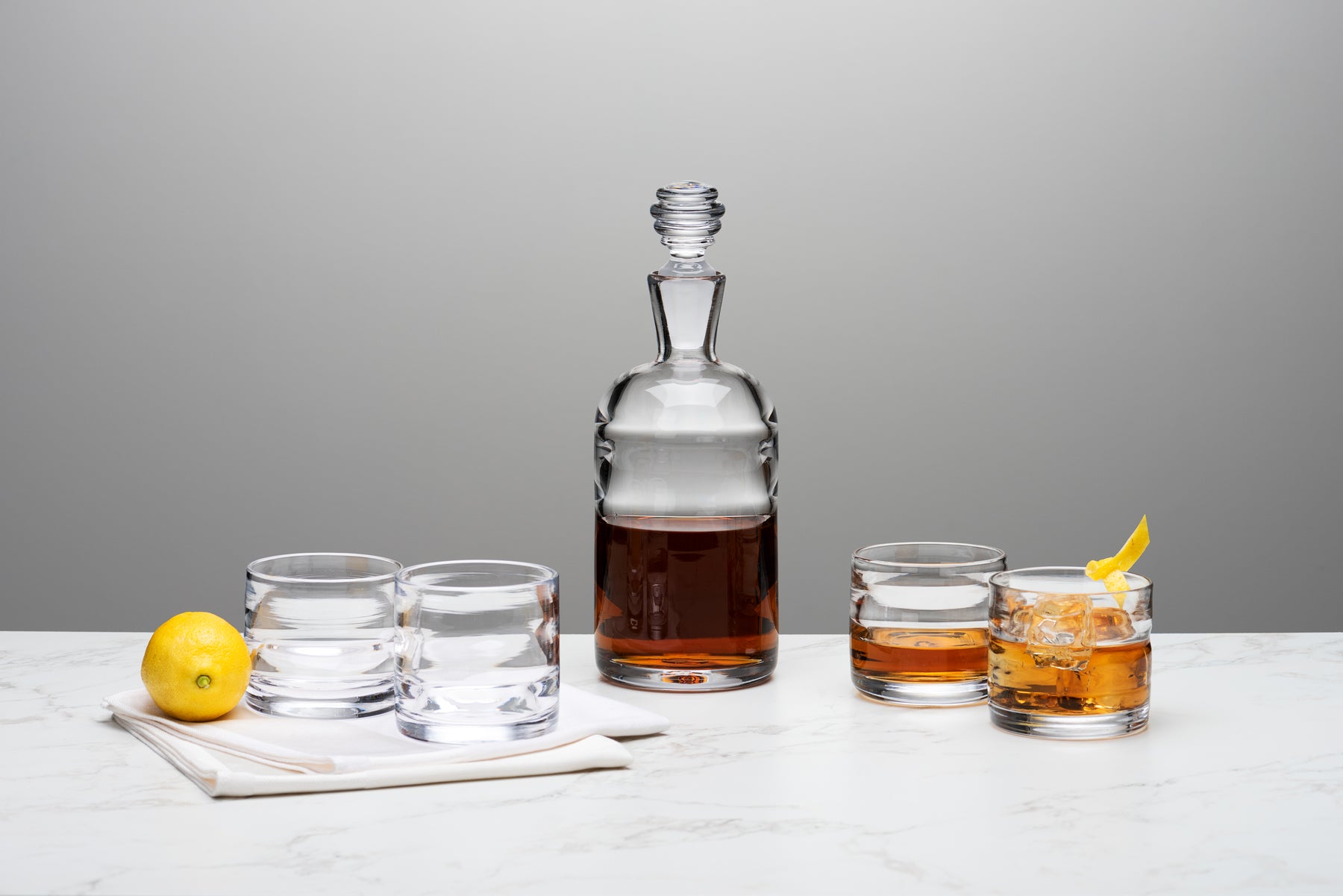 The Small Batch Glass Lighthouse series decanter and rocks glasses sit atop a marble table against a grey background. Image by Loam