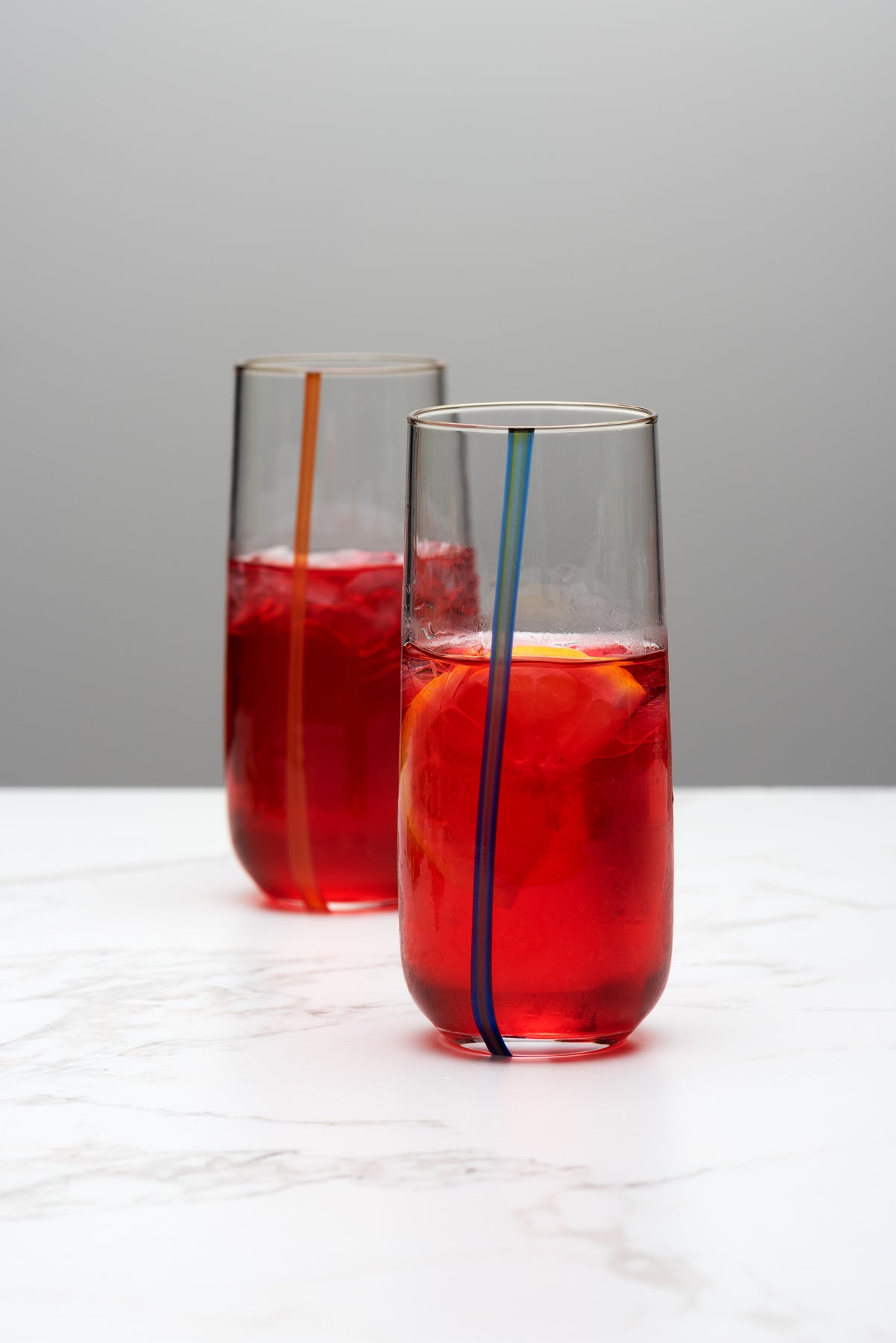 two stemless flute glasses hold a bright pink liquid on a marble table top. Image by Loam