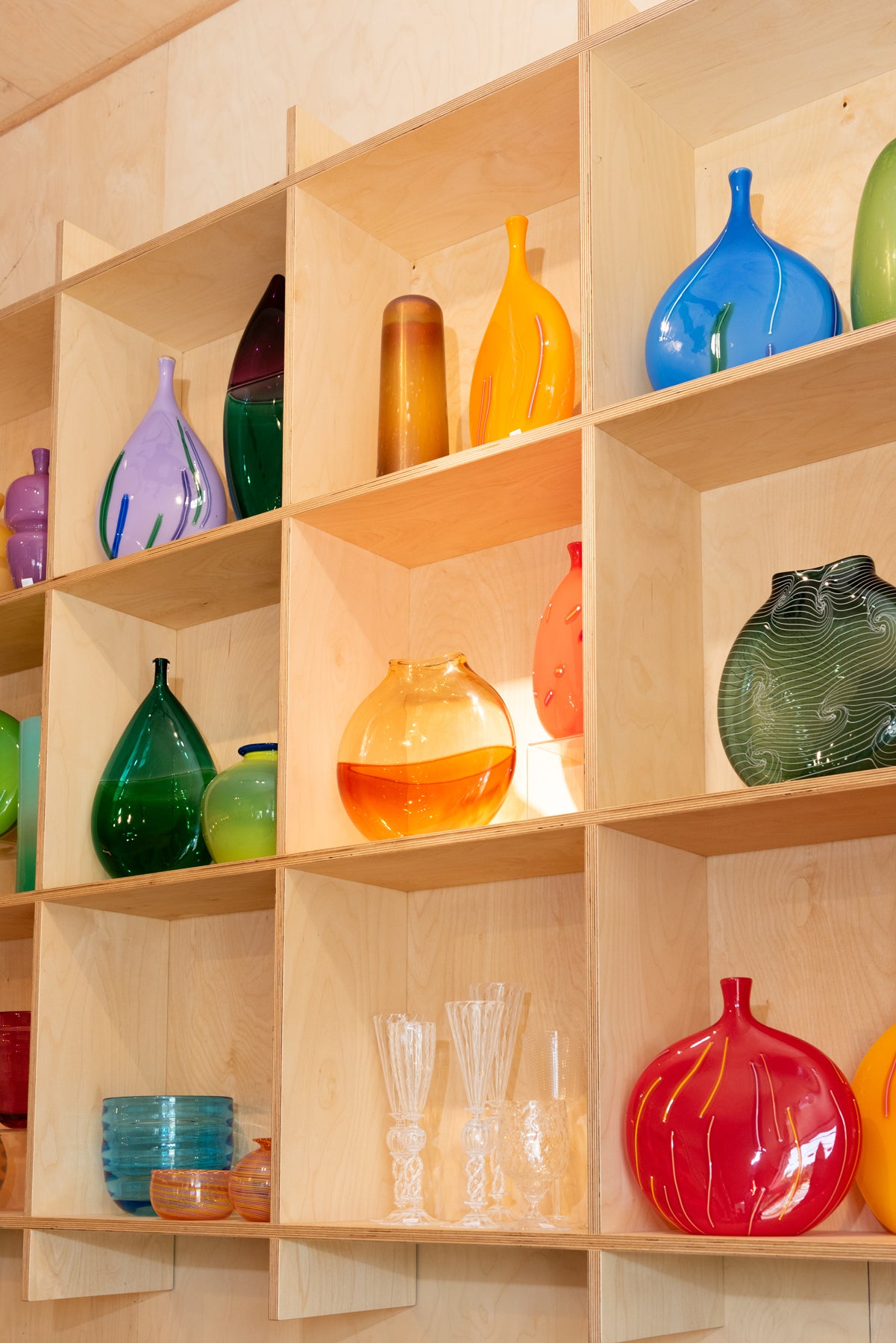 A gallery view of a grid wall in the Small Batch Glass gallery where varied hand blown shapes sit. Image by Loam