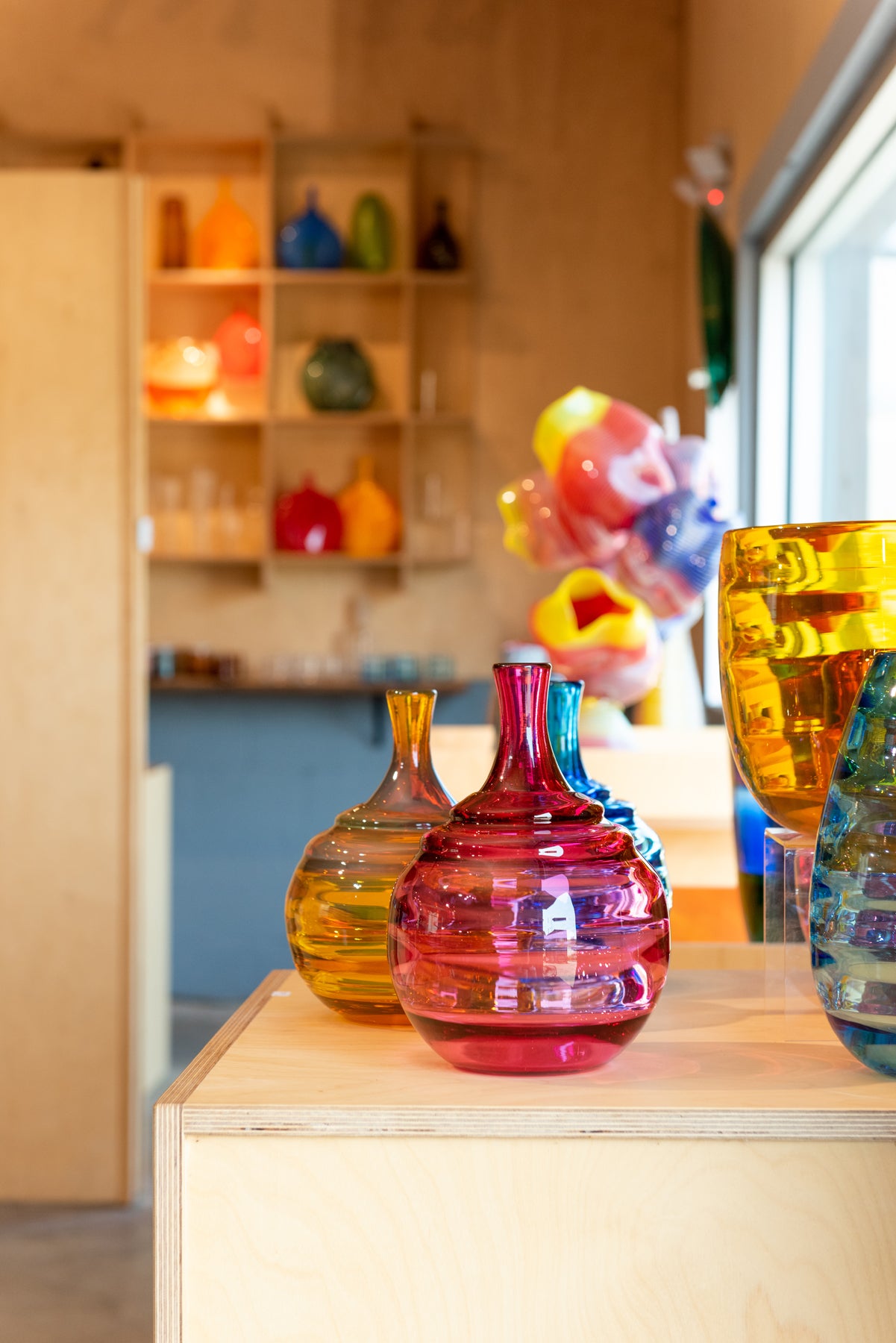 A view inside the Small Batch Glass gallery in Asheville of some brightly colored glass vases with more work in the background. Image by Loam