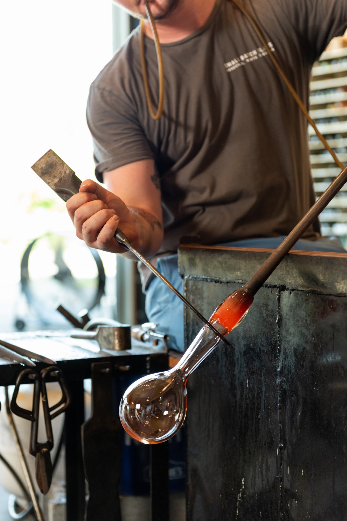 Asher Holman tooling a piece of hot glass that is held at an angle in the Small Batch Glass hotshop. Image by Loam