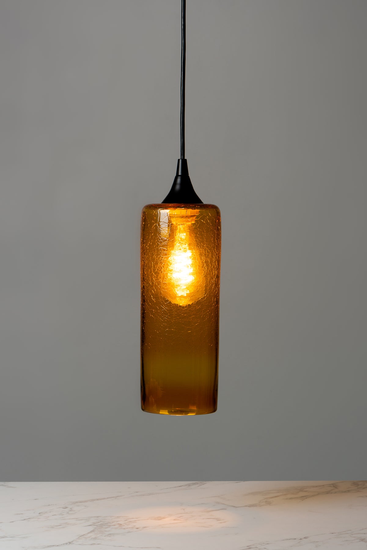 An orange cylindrical pendant light in a deep rusty orange hands above a table top. Image by Loam