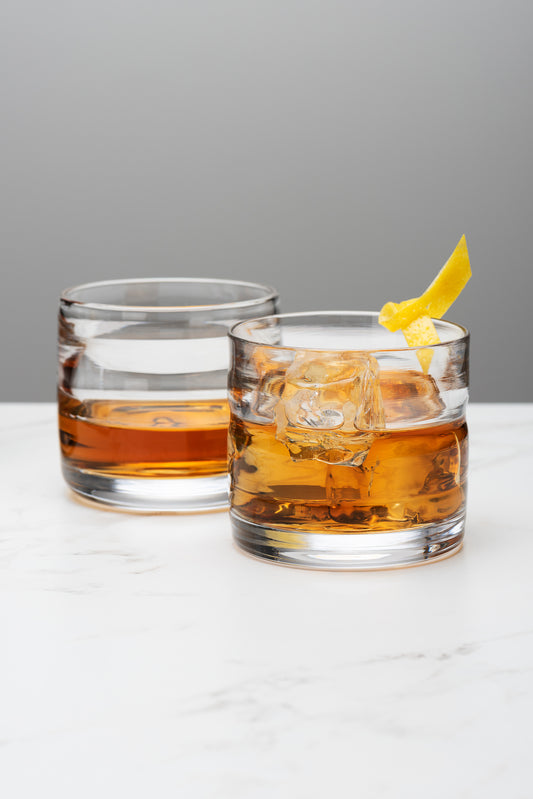 two thick rocks glasses holding ice and whiskey sit atop a marble table top. Image by Loam