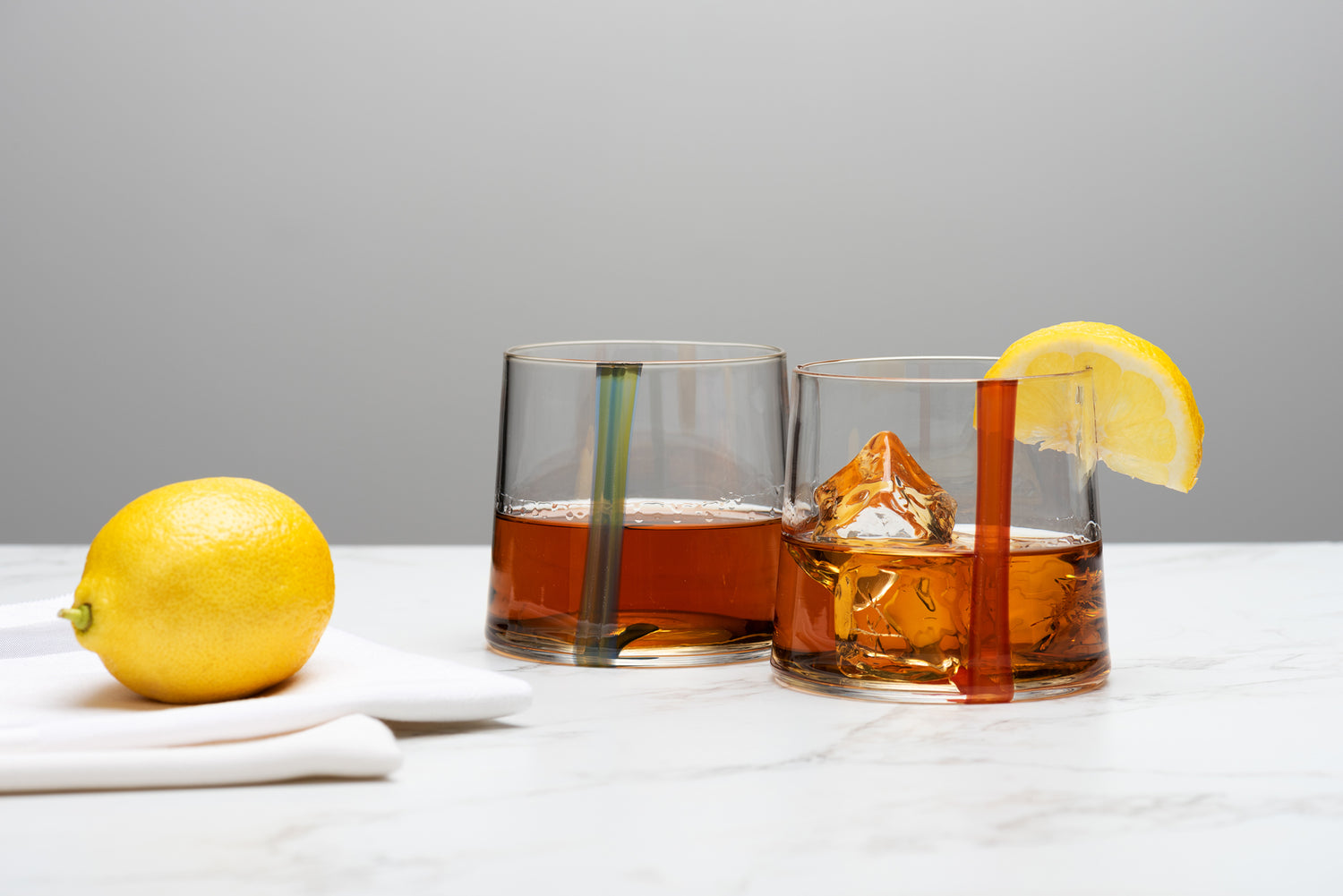Two Small Batch Glass rocks glasses sit on a marble table with ice and whiskey and a lemon. Image by Loam