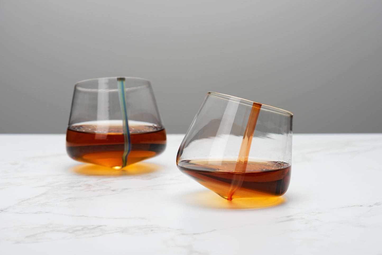 Two stemless snifters with rounded bottoms sway on a marble table. Image by Loam
