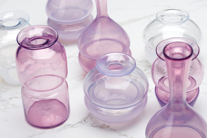 A close up of pink and purple and clear busvases sit on a marble table top.Image by Loam