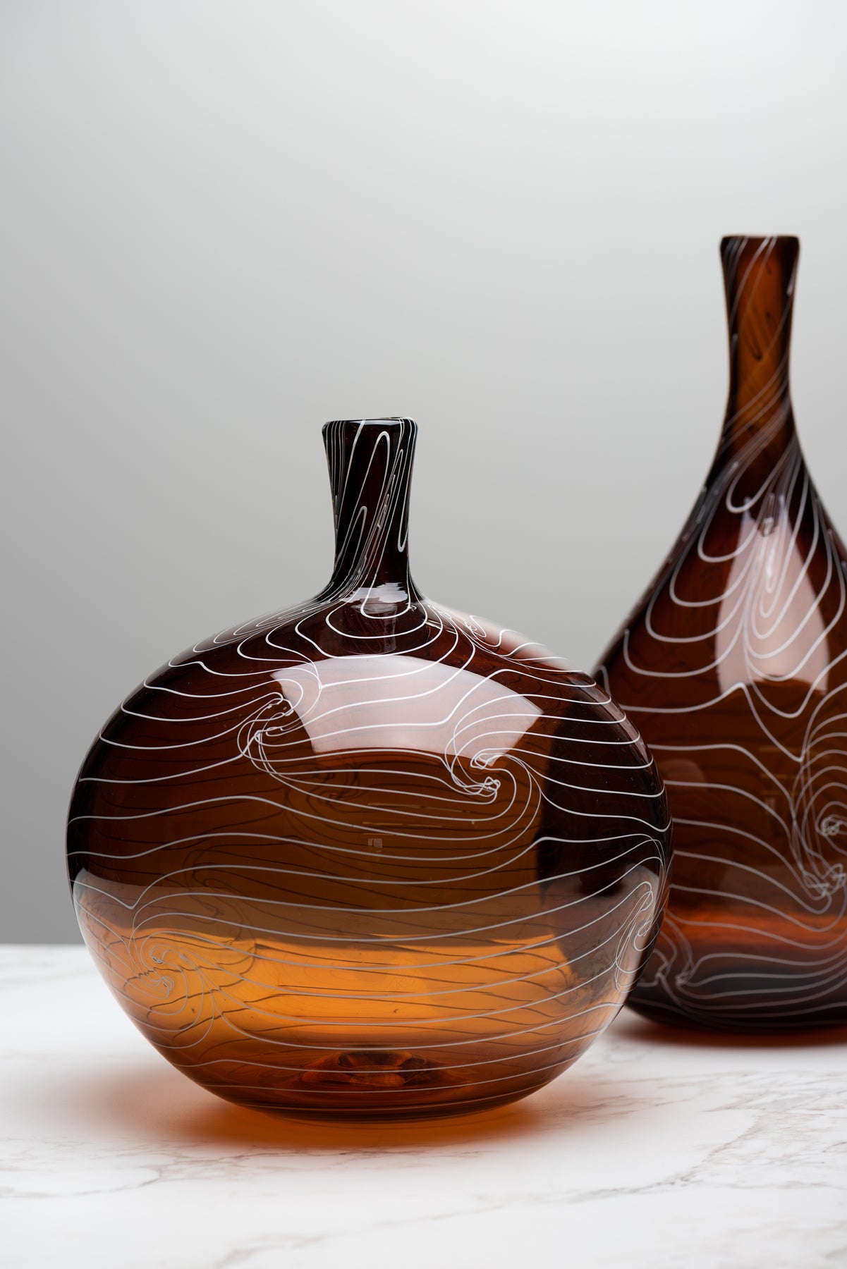 Two deep brown bottles by Small Batch Glass sit on a marble table against a grey background. Image by Loam
